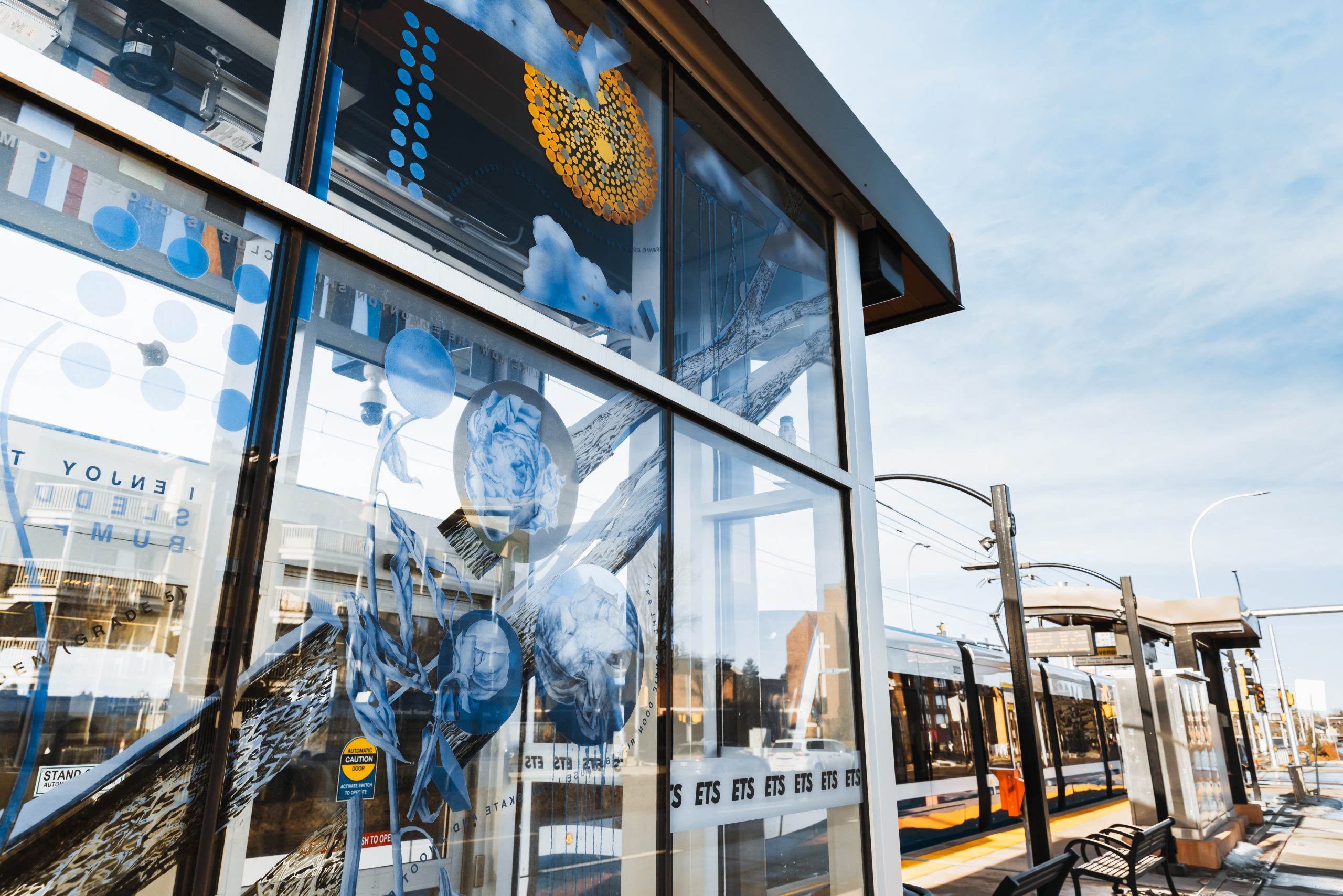 Windows of a LRT shelter are decorated with art of blue flowers, trees and dots.