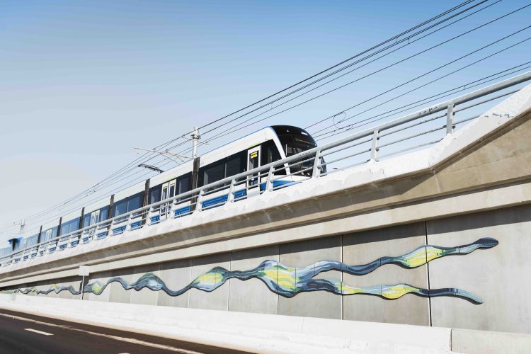 An LRT speeds along a concrete ramp decorated with mosaic tiles arranged in the pattern of a two-tailed comet.