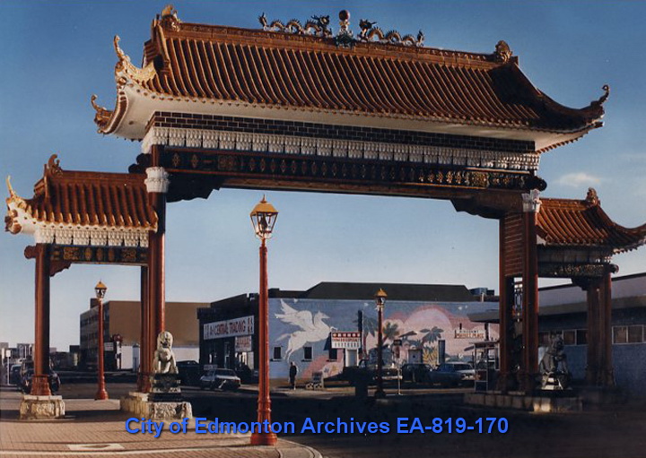 A large pagoda-style gate, guarded by two lion statues at the base and topped with two dragon statues, spans a city street.