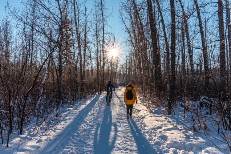 Two people walking on a winter trail with the sun setting in the background.