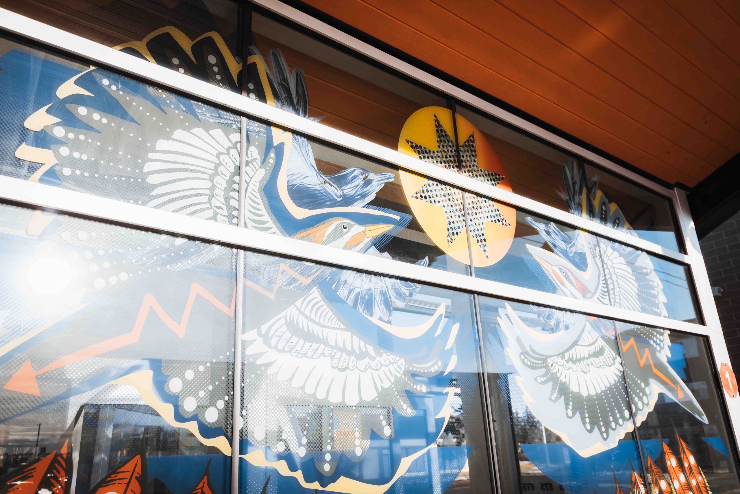 The windows of an LRT station are decorated with images of two birds, feathers and a star.