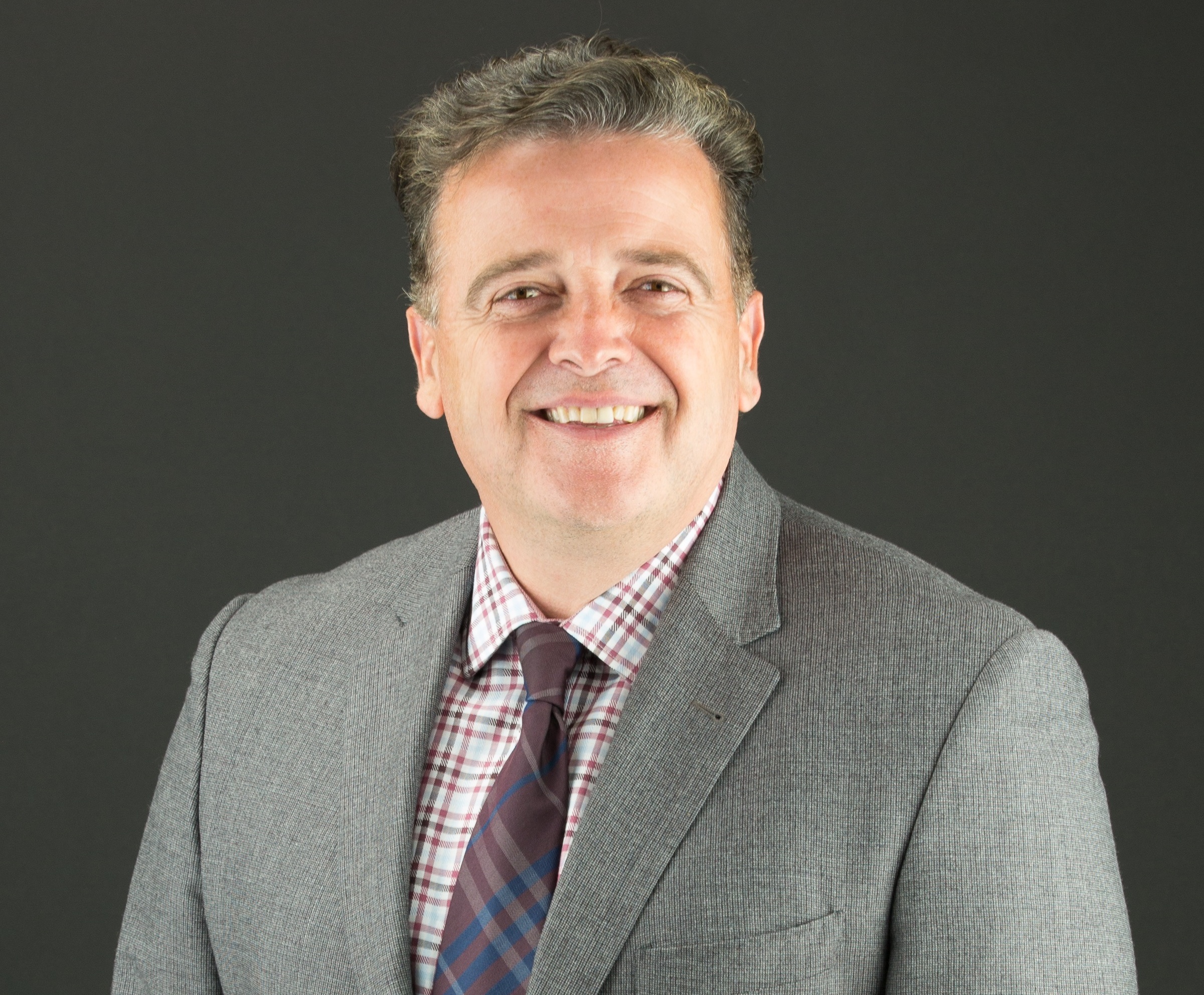 A smiling white man with salt and pepper hair and a gray suit.