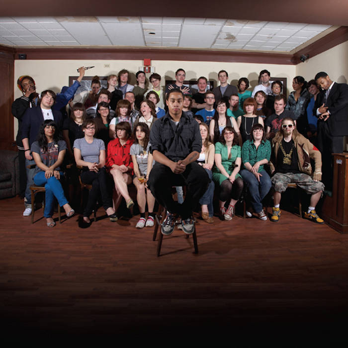 Cadence Weapon sits on a stool in front of 30 of his friends seated in chairs. Credit: Upper Class Recordings