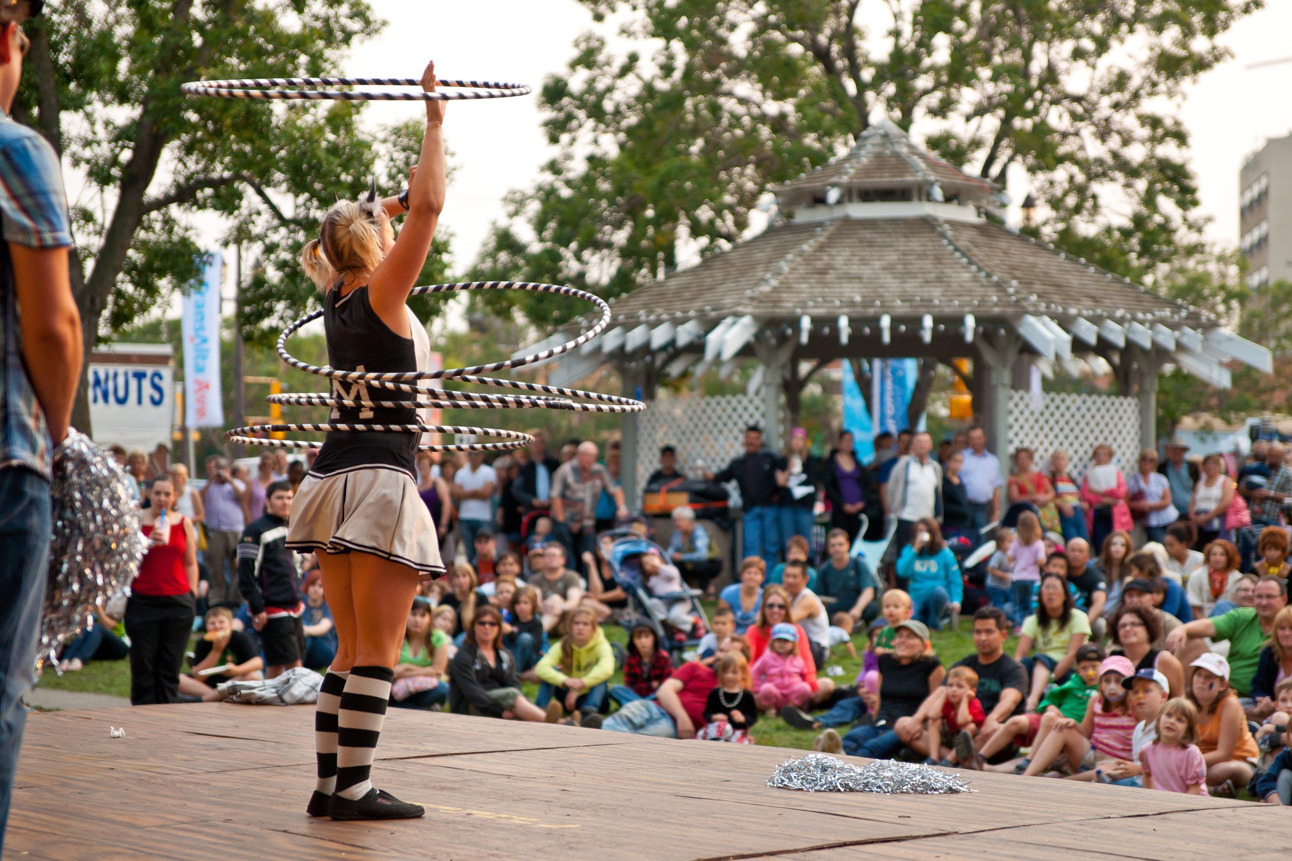 A hula-hoop performer on stage in front of a crowd in a park.