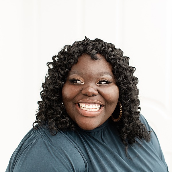 Sarah Adomako-Ansah wearing a green shirt in front of a white background is smiling and looking to the left.