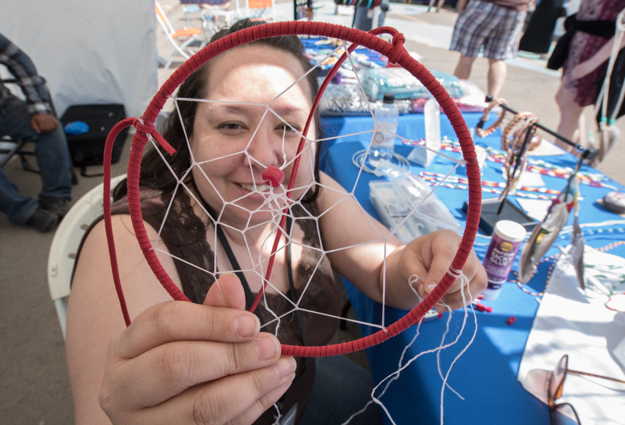 An Indigenous artist making a dreamcatcher while at booth at the Downtown Market outdoors.