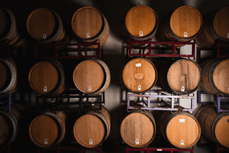 Three rows of wine wooden barrels stacked on top of each other. The lighting is darker on one side and lighter on the other.