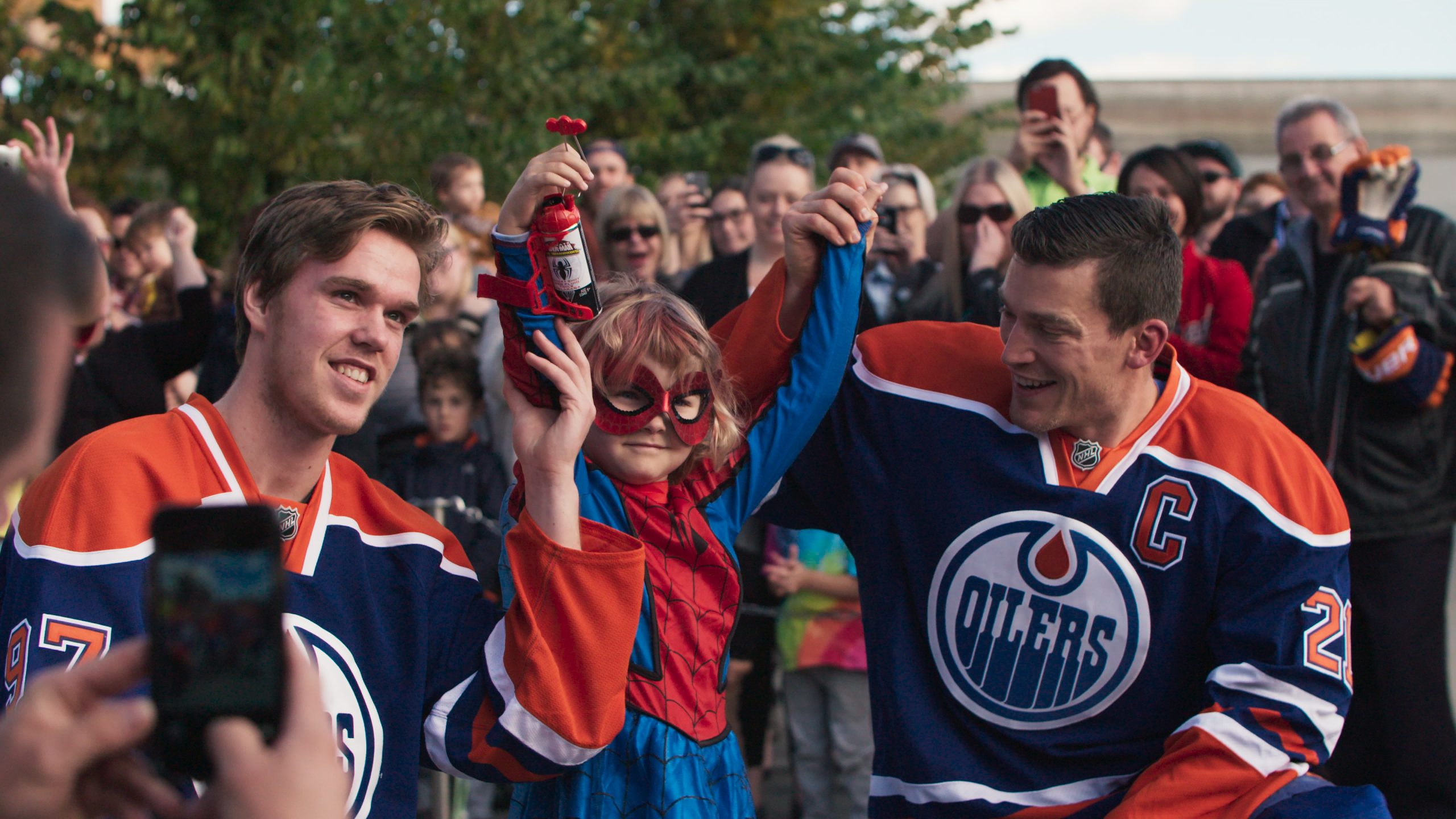 A scene from SpiderMable with 2 hockey players celebrating with her with a crowd cheering