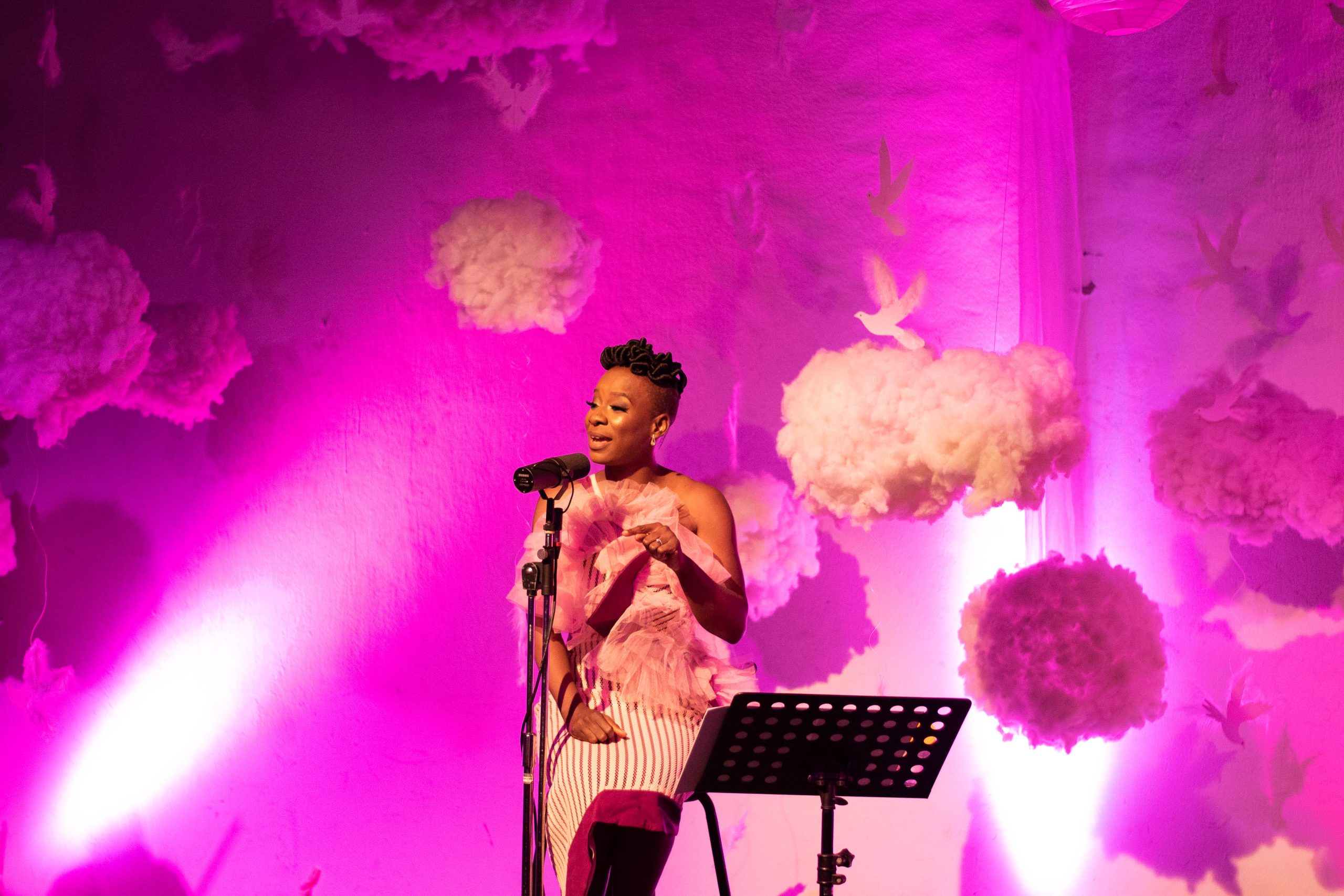 A woman sits on a chair as she performs her poetry on stage.