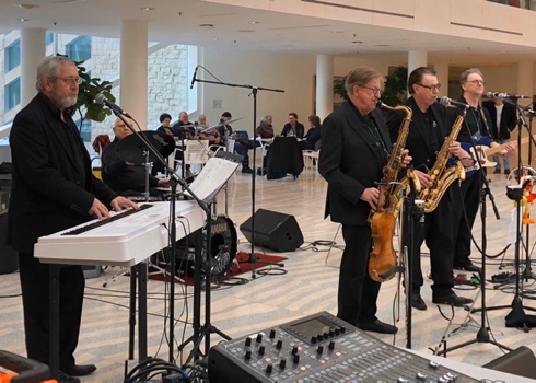 The band, The Emeralds, performing inside City Hall. Members are playing a piano, saxophones and a guitar.