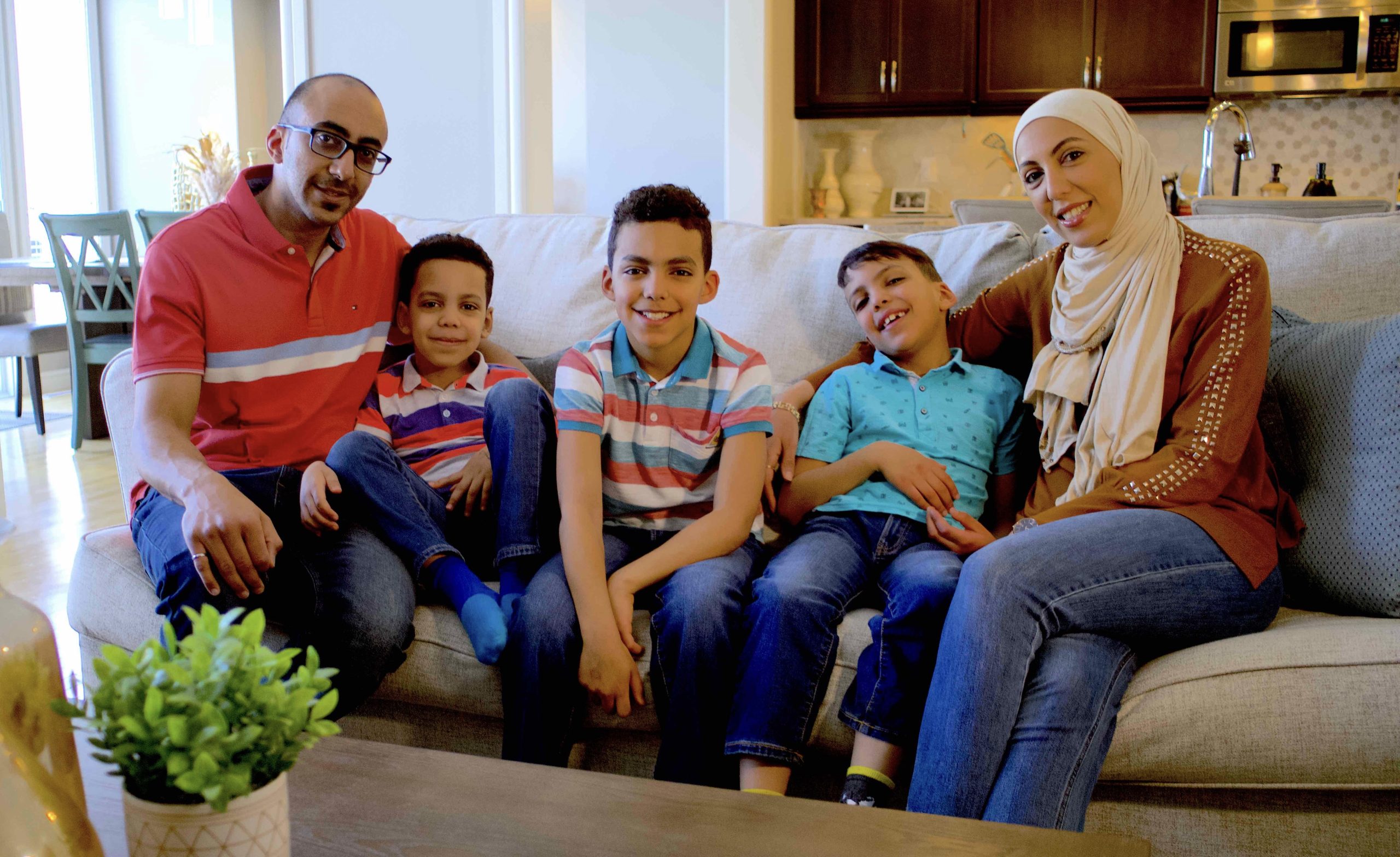 A family with 3 children sits on a couch inside their home.