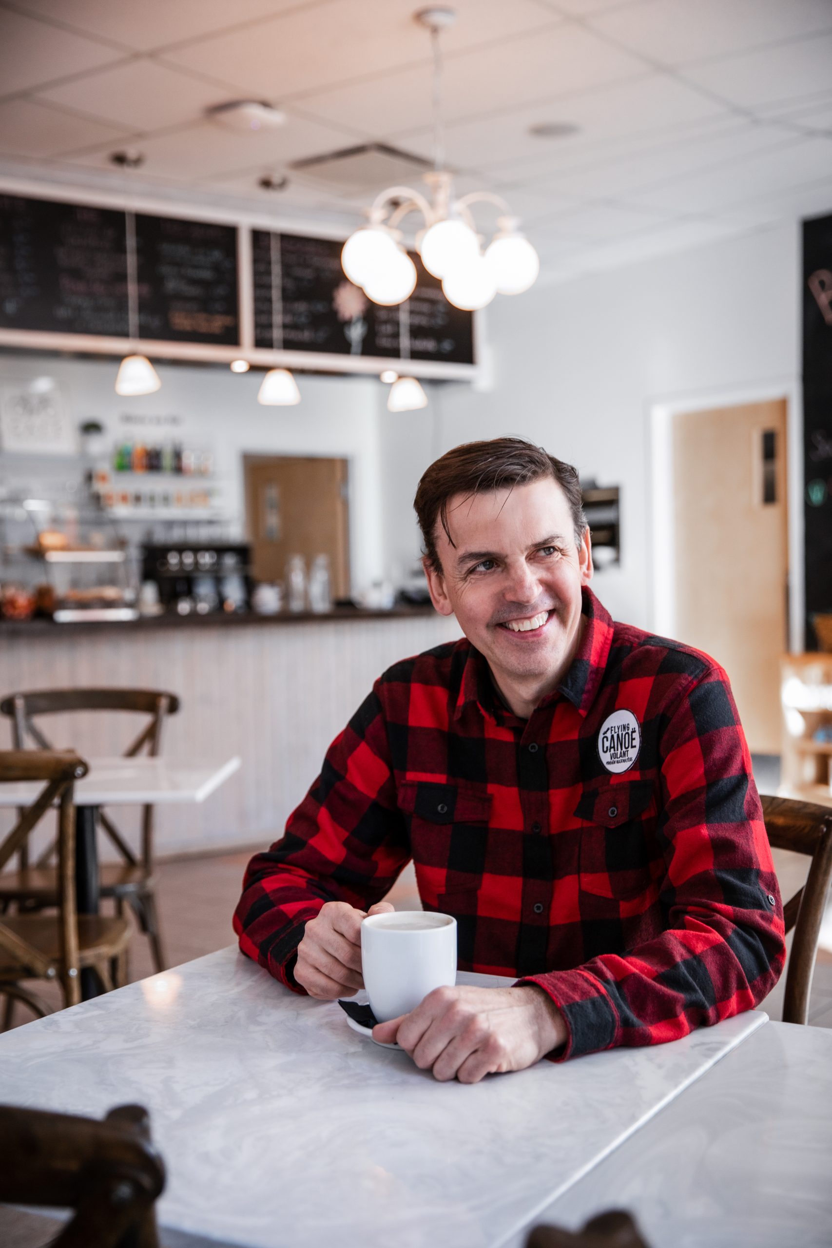 Daniel Cournoyer, wearing red plaid, sits in his restaurant, Café Bicyclette, while drinking a coffee.