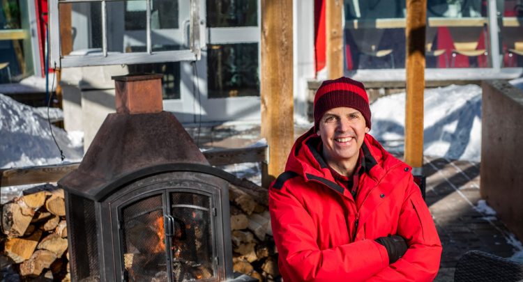 Daniel Cournoyer poses in a red winter jacket in front of a fireplace on the Café Bicyclette patio in the winter.