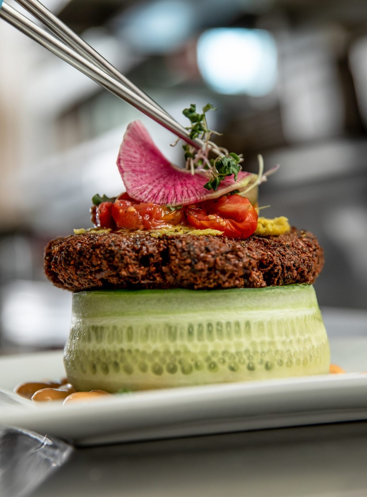 Sprouts being placed on top of the Jardin Bicyclette dish made of cucumber, falafel patty and tomatoes.