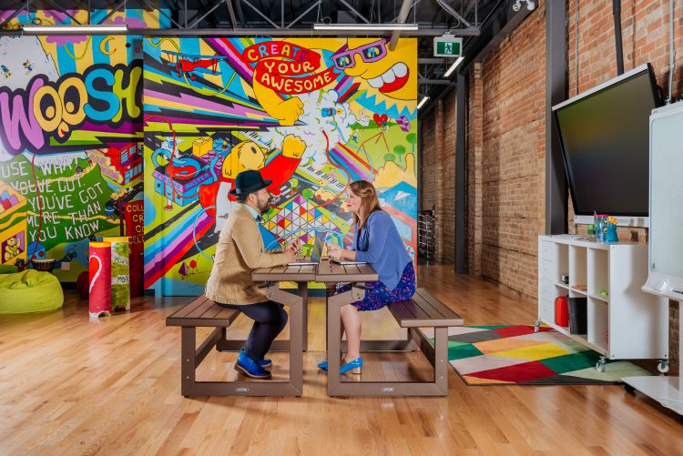 CEOs sitting at desks in colorful office warehouse at local business Qi Creative