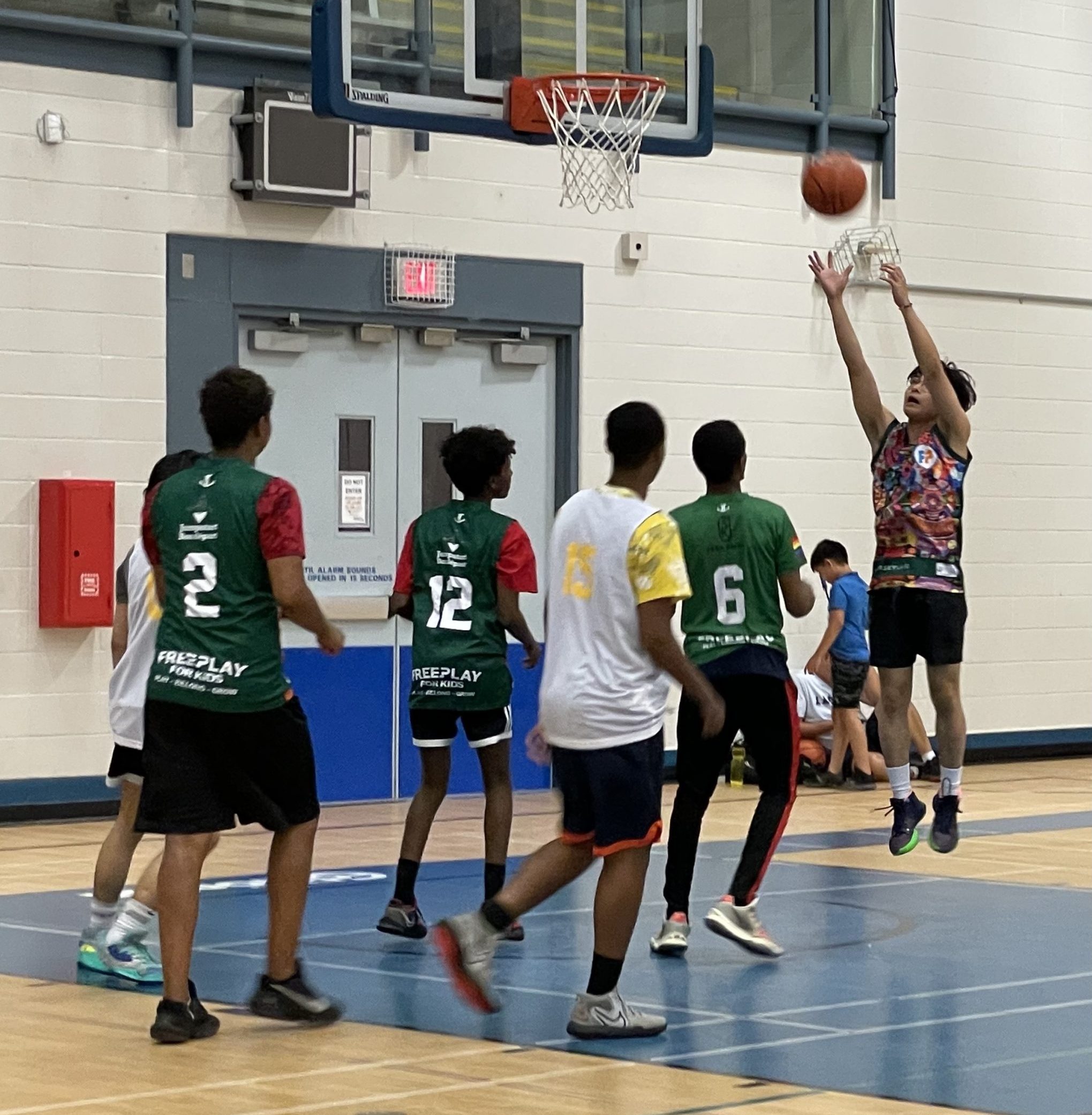 A group of teens playing basketball in a gymnasium.