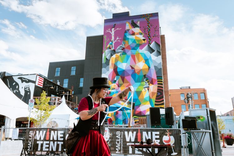 A magician performing at Fringe Festival 2022 in front of the Okuda Mural in Old Strathcona