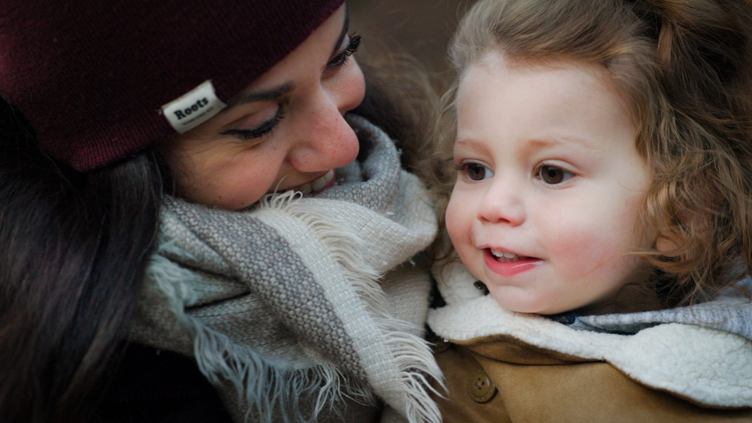 A close up of a mother holding a child. Both are dressed in winter clothes.