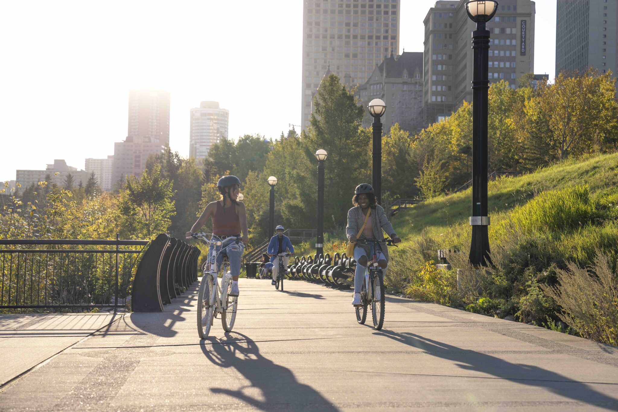 Three people cycling in the river valley with skyscrapers in the background.