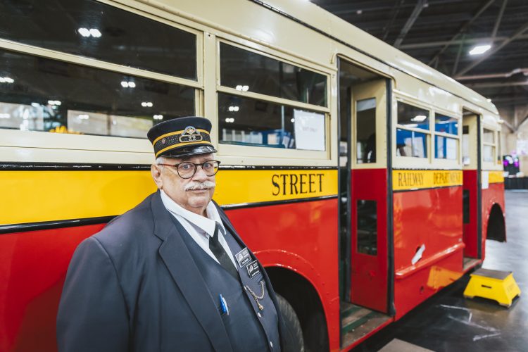 A man in an ETS uniform stands in front of a vintage bus with yellow, red, and beige colors.