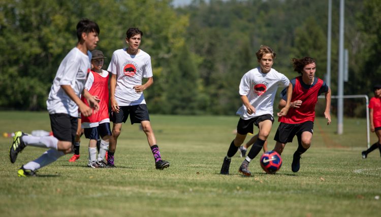 Young male Indigenous soccer players chase after a ball on a field.