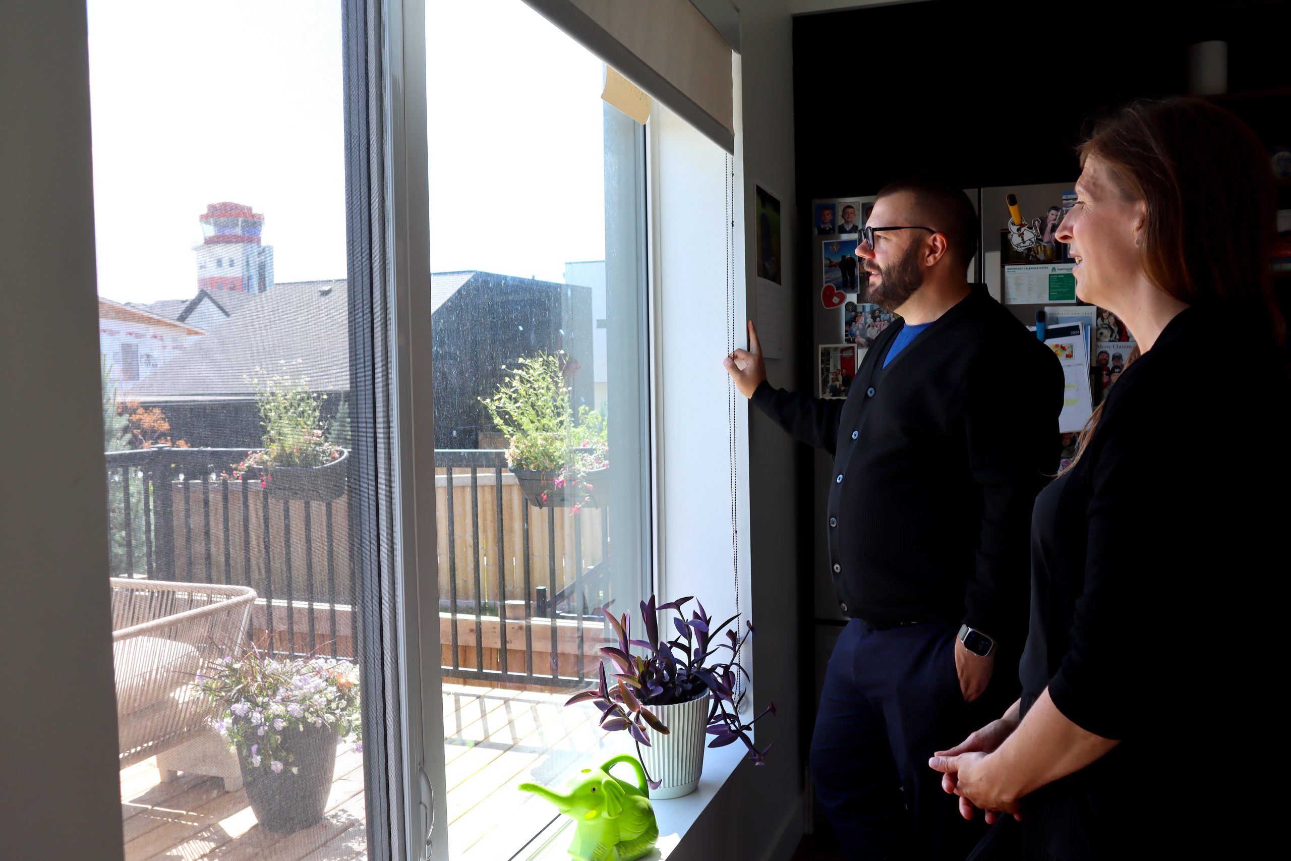 A man and a woman lookout a back sliding door window out onto a deck with planters in the background