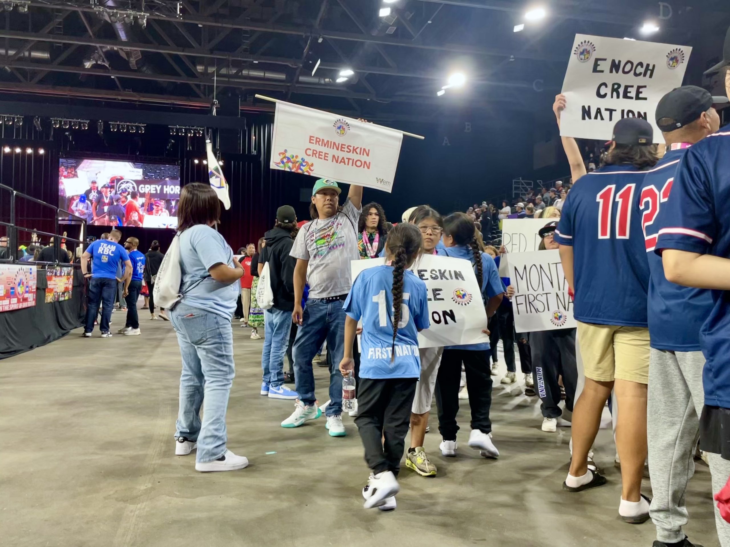 Young Indigenous athletes hold signs with the names of Indigenous communities inside a small arena.