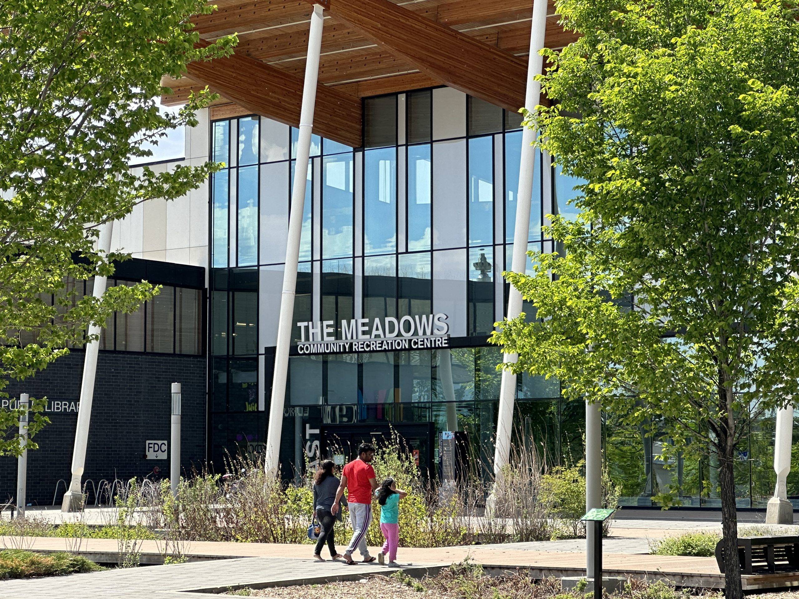 A father, in between two children, walk towards the main entrance of The Meadows Community Recreation Centre.