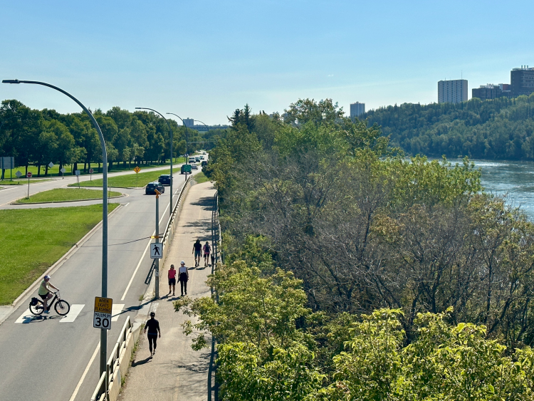 Ariel shot looking down at people walking and cycling near Edmonton's river valley with lucious trees are framed by the North Saskatchewan River on the right.