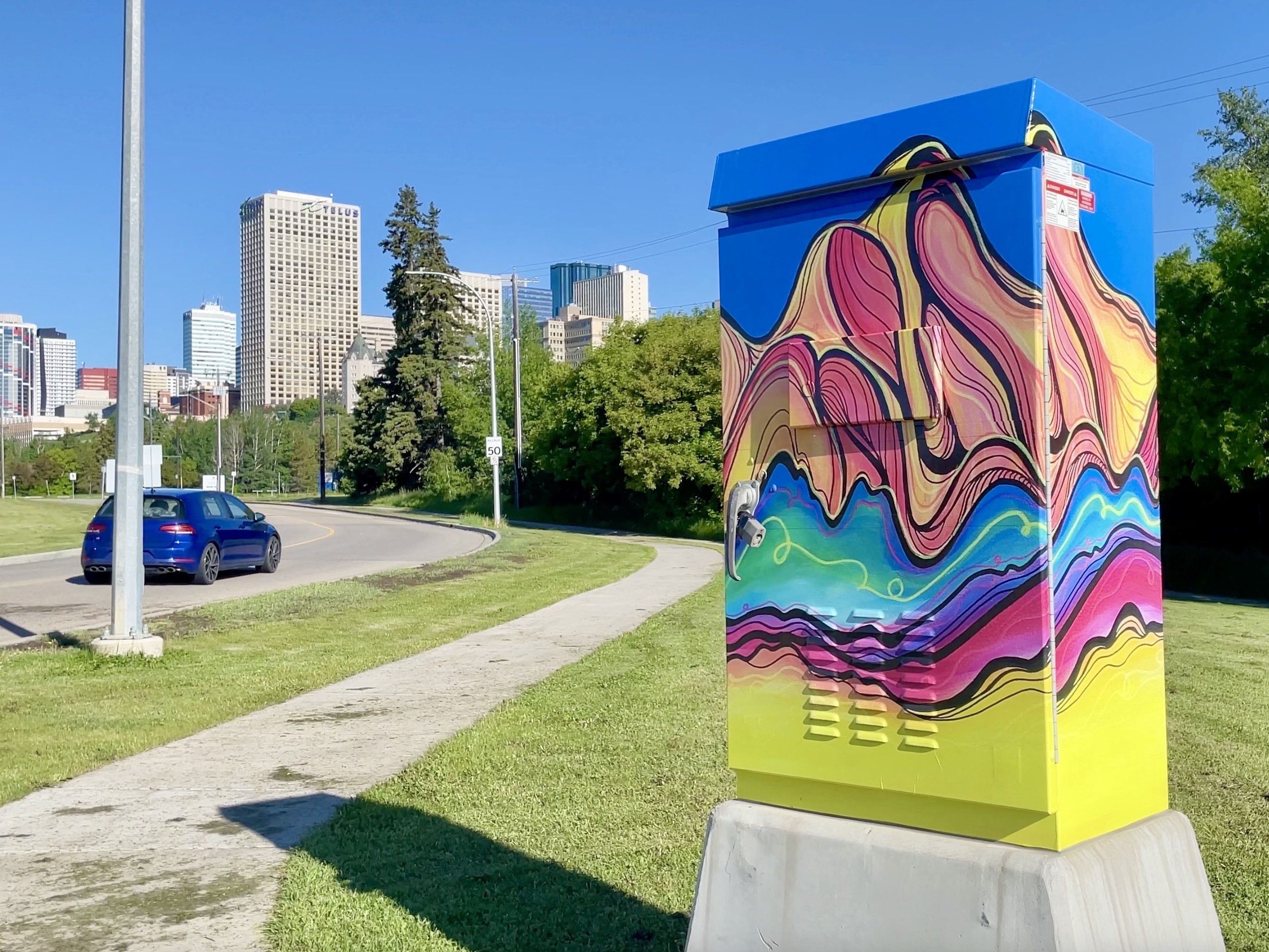 A car drives by a control box wrapped with a design of a wavy mountain.