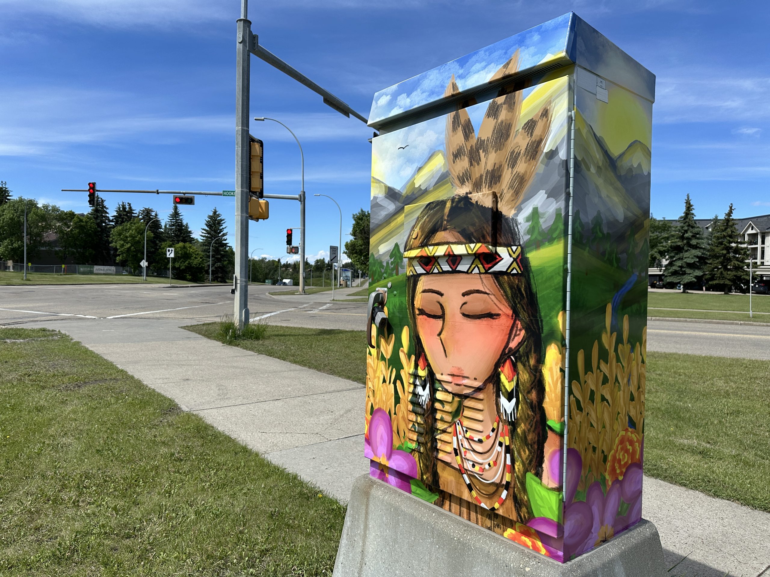 A traffic control box, featuring artwork of a young Indigenous girl wearing feathers, earrings and necklaces, stands near an intersection.