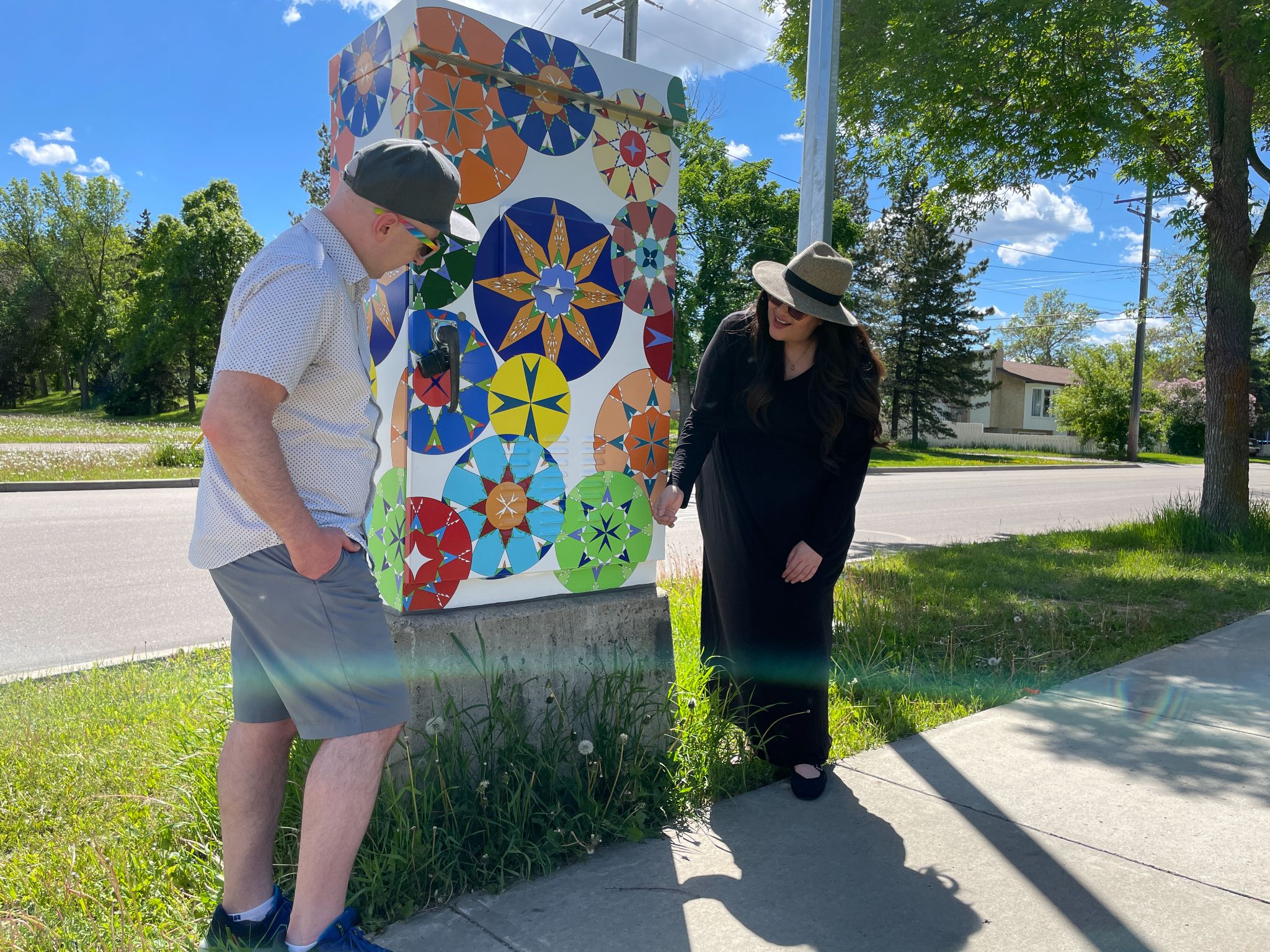 A man and woman look at a traffic control box wrapped with artwork featuring kaleidoscopic circles.