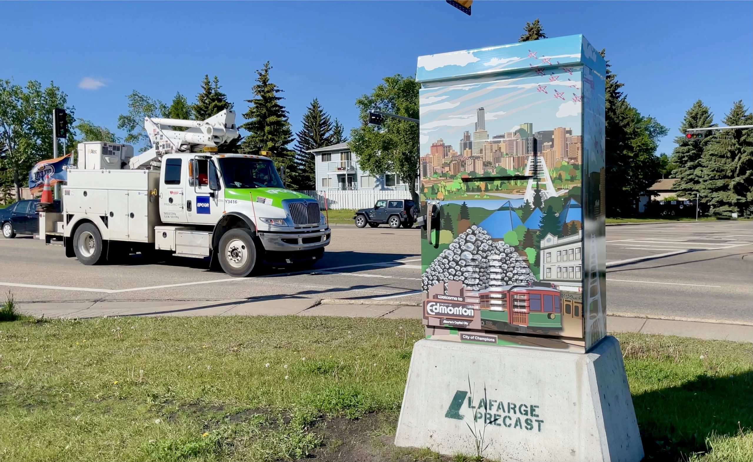 An EPCOR truck drives by a traffic control box wrapped with artwork of the downtown skyline, Walterdale Bridge, Muttart Conservatory, Fort Edmonton Park and Talus Dome.