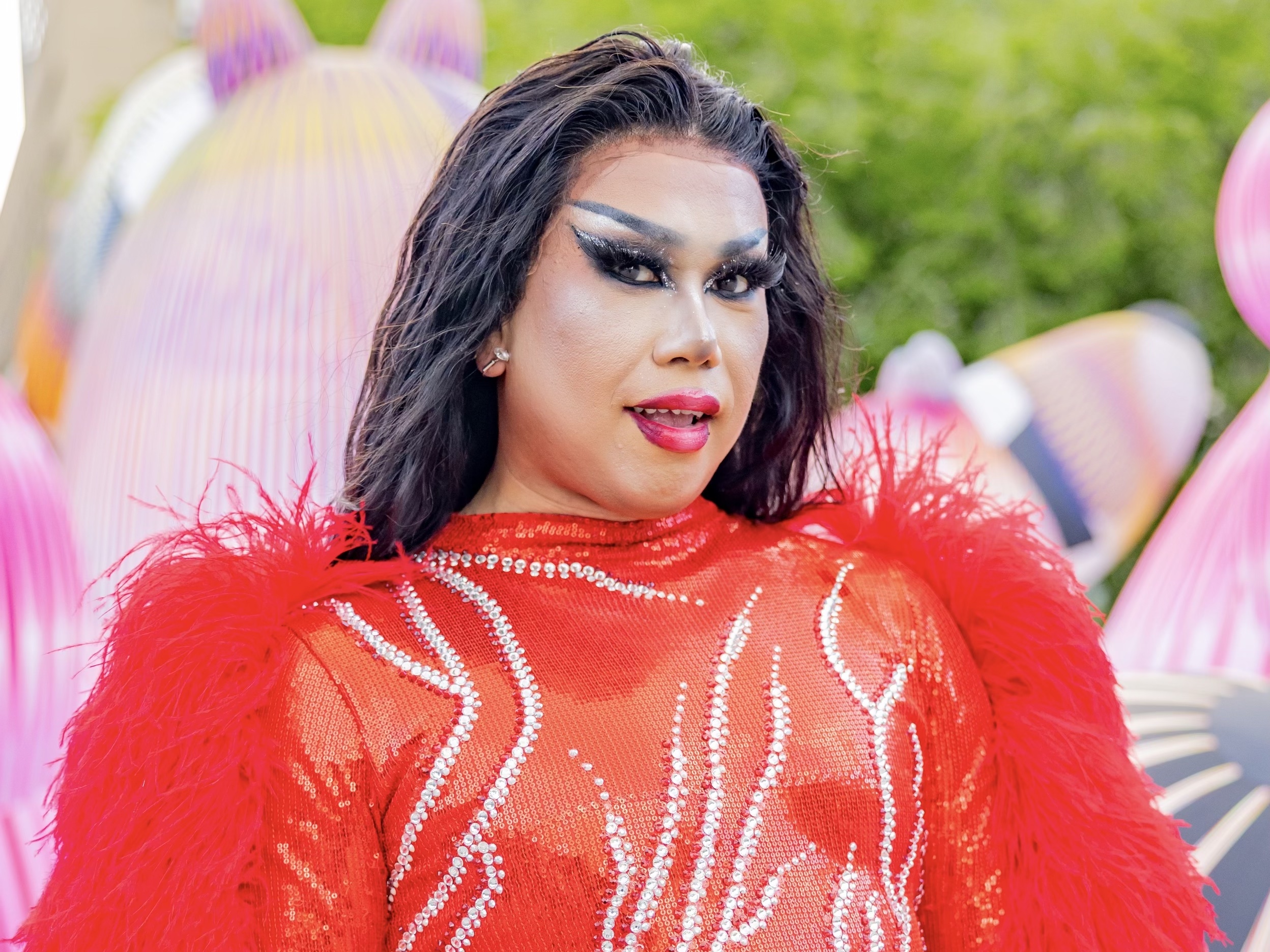 A drag queen poses in a red bodysuit adorned with flowers and crystals.