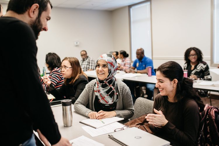 Two women animatedly learning from an instructor in a classroom