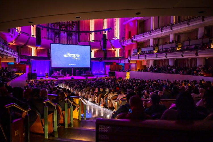 A dark theatre with all of the seats full. A screen at the front says "The Mosquers Film Festival".