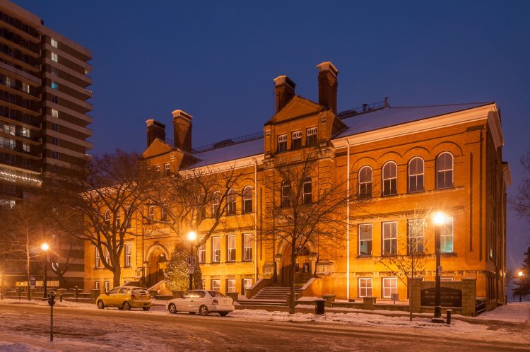 The exterior of a large, historic 4-story brick building with two grand entrances and four chimneys, with street lights on a winter night.