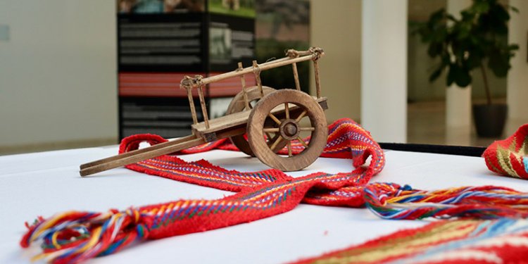 A long red and colourful-striped scarf sits on a table with a small wooden wagon.