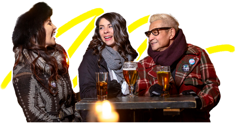 Cut out of three people sitting at a table, laughing, with drinks on the table in front of them. There is a yellow squiggle accent behind them.