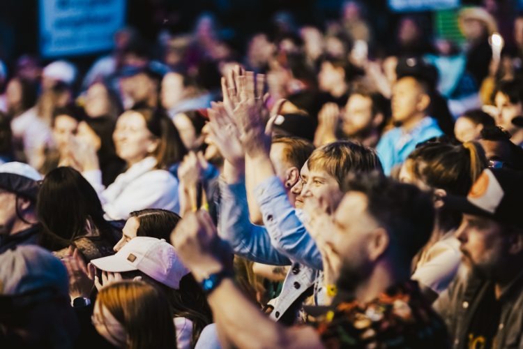 Audience members enthusiastically clap and cheer, their faces lit with excitement, in a lively, crowded Edmonton Folk Festival.