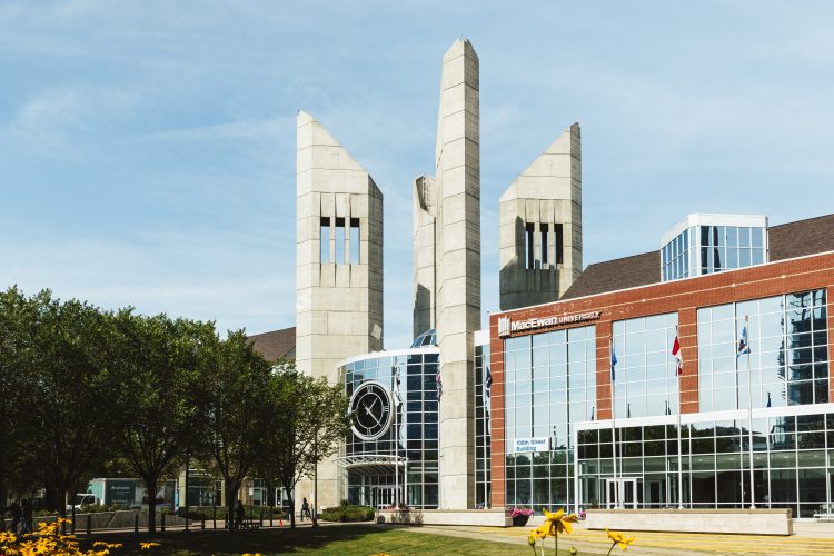 A brick and glass building featuring four concrete 2-story towers on a sunny day.