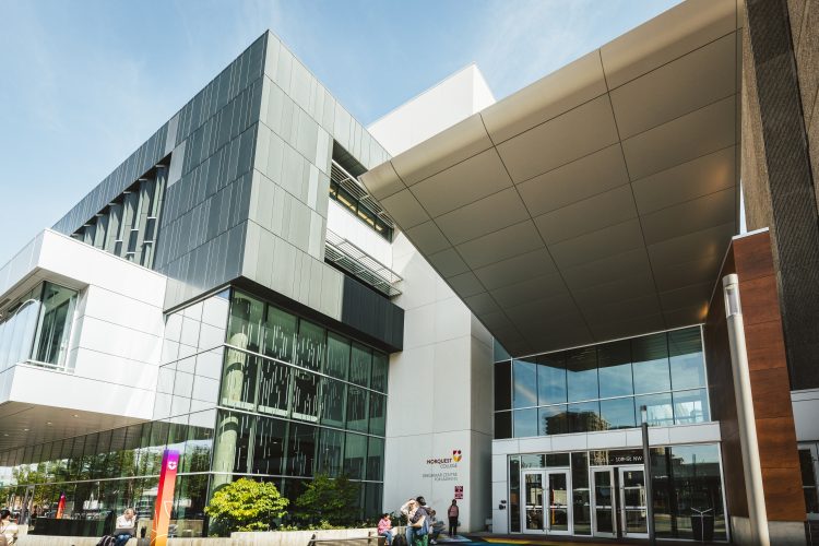 Front entrance of a 4-story college building with several square outcroppings in diverse materials.