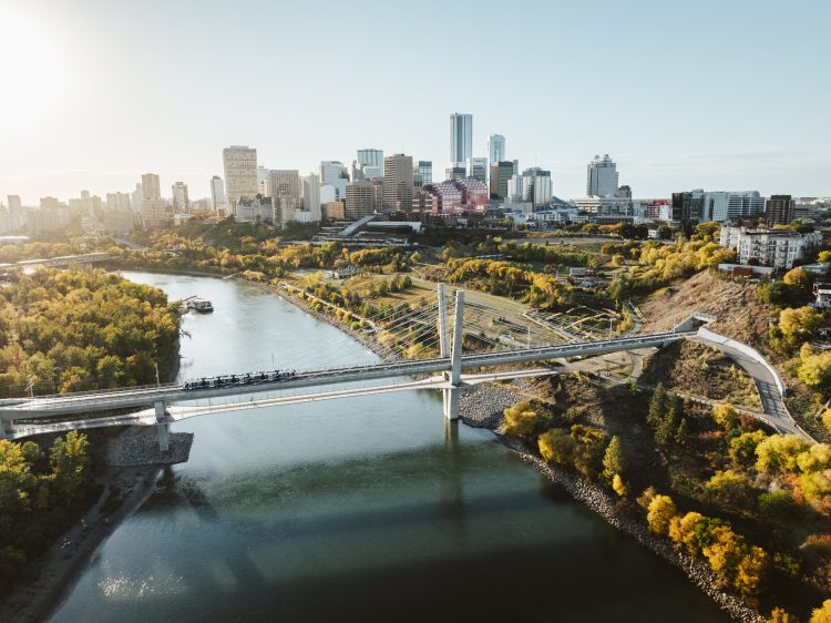 Aerial of an 4-car train crossing a bridge over a river with downtown buildings in the background