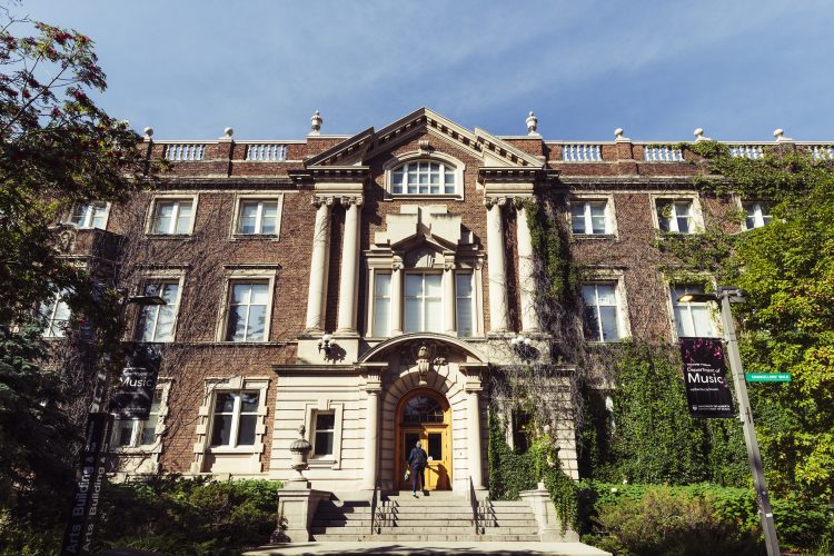 A person walks into 4-story historic brick building with vines growing on it on a sunny day.