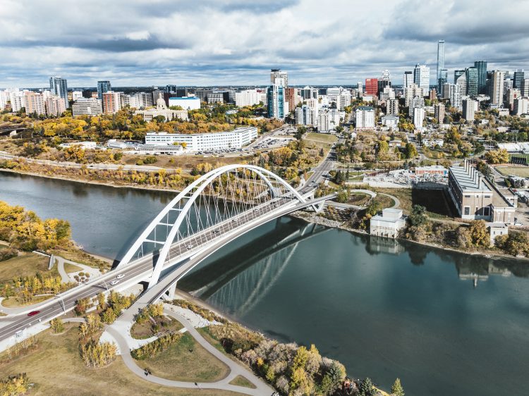 A large white arched bridge across a river in a fall river valley with the downtown skyline.