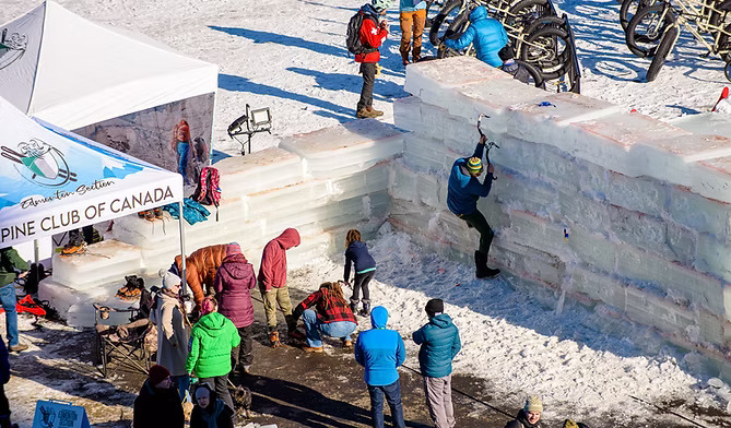 An overhead view of families playing around a small ice wall at a festival on a sunny day.