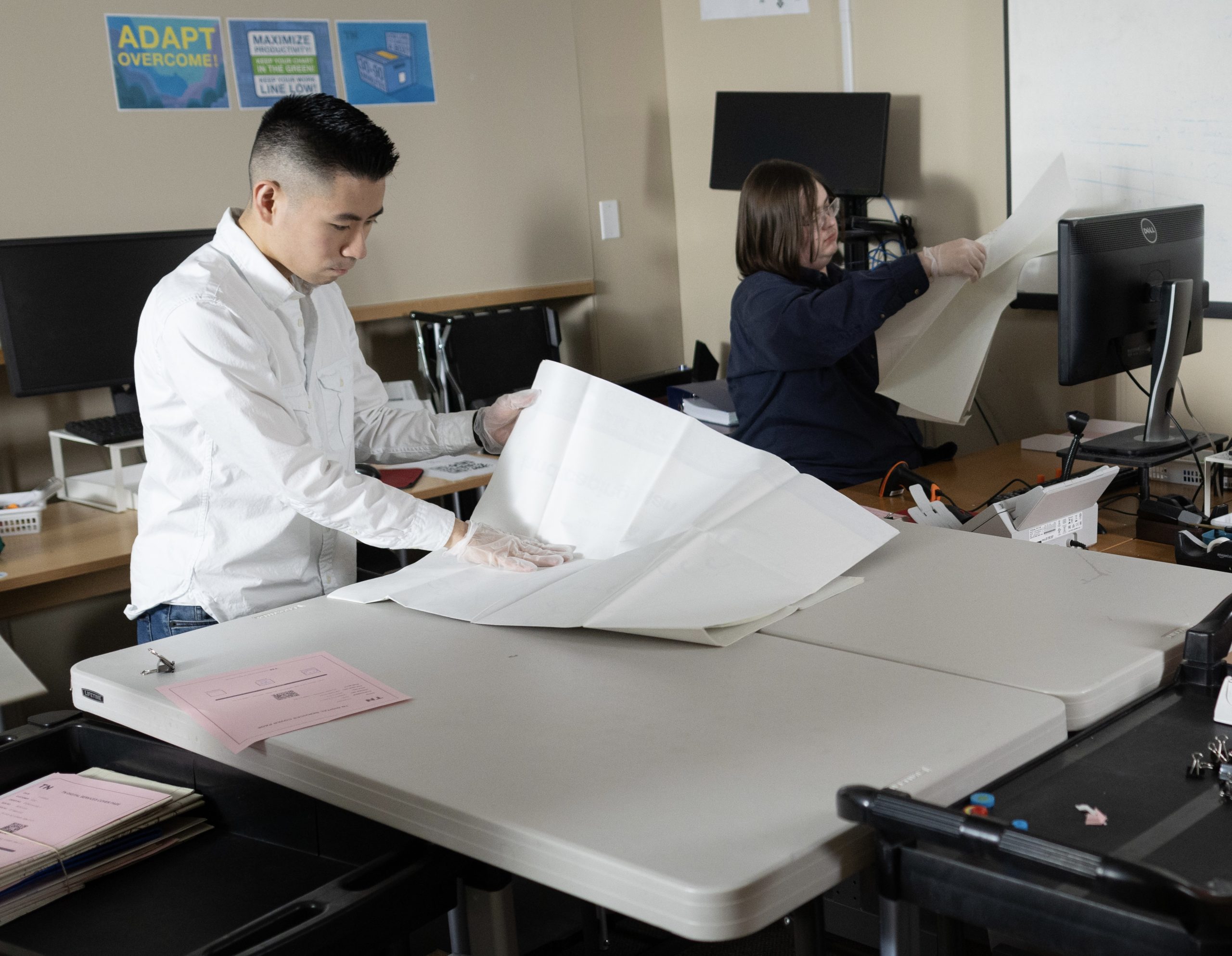 Two men hold sheets of paper in an office space.