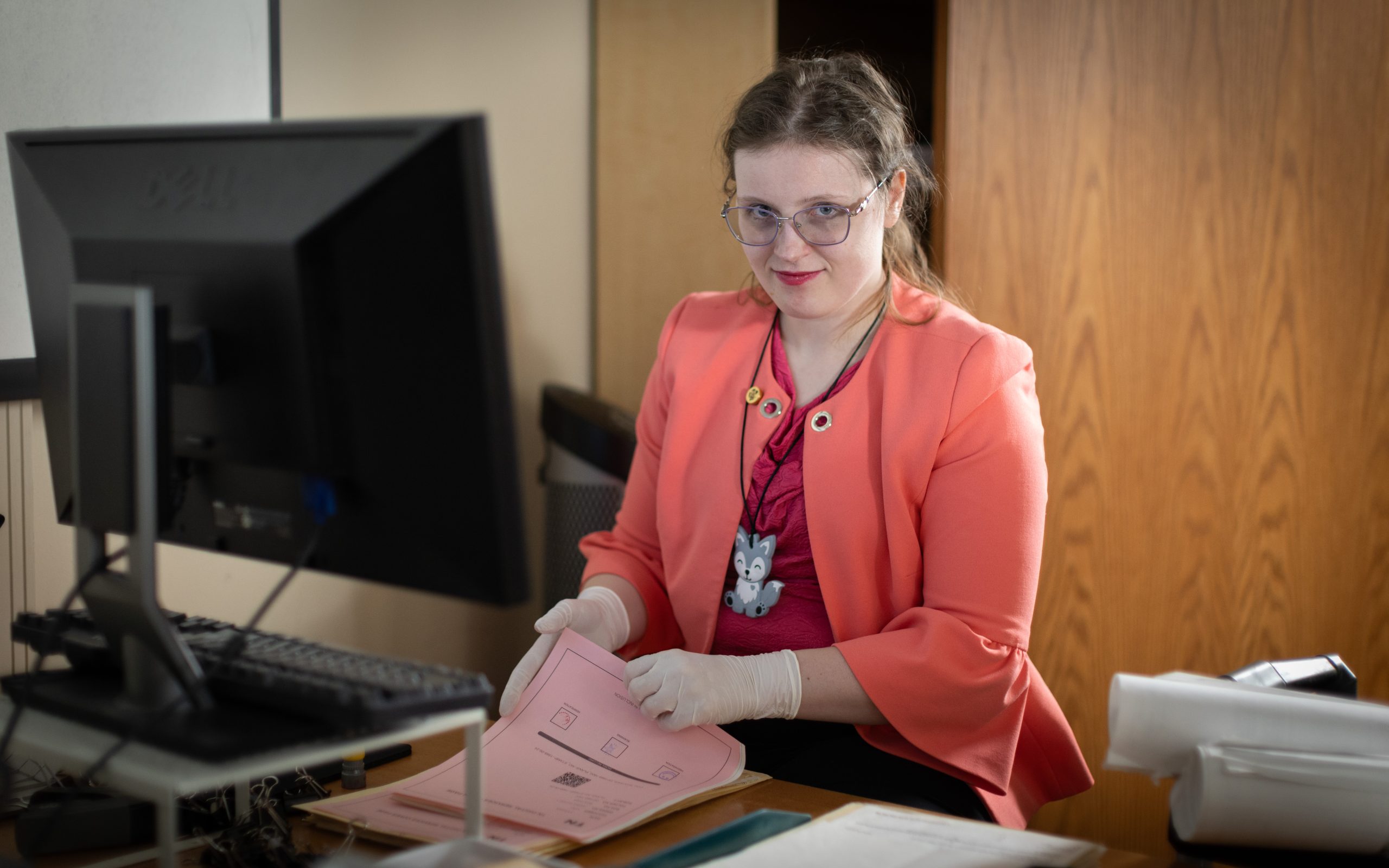 A woman sits in front of a computer, holding some paper in her hands.