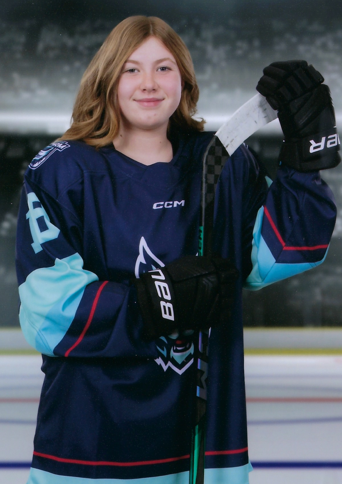 A 12 year old girl in a dark blue hockey uniform, holding a hockey stick