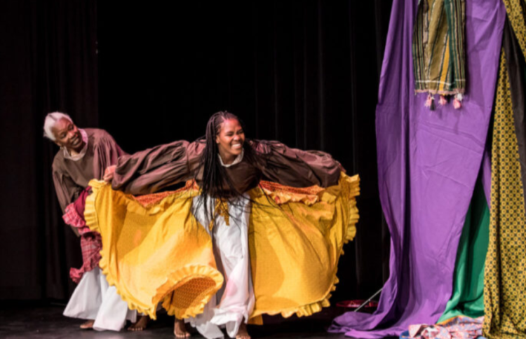 Two black women dressed in colourful costumes perform on a stage.